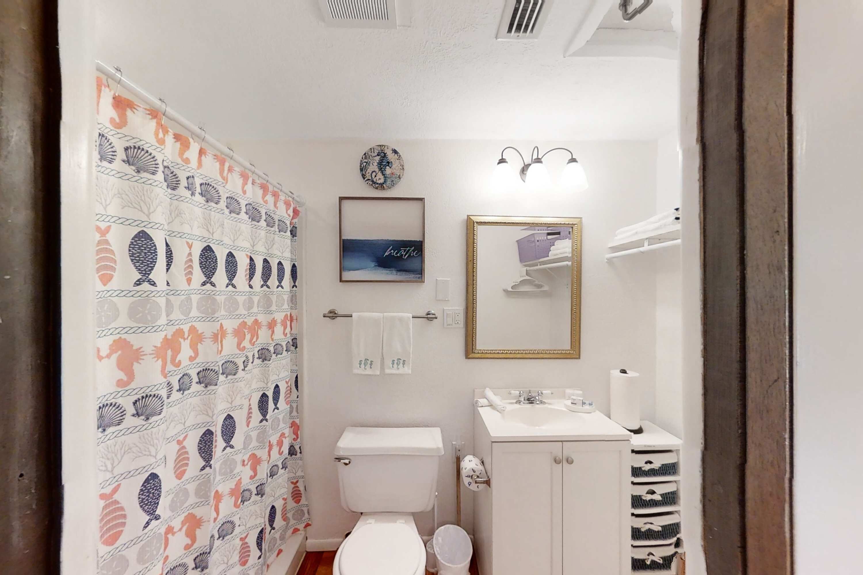 Et badeværelse med toilet, vask og bruseforhæng med fiskemønster.