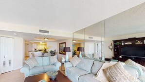 A living room with a sofa, coffee table, and a television. There is a kitchen area in the background.
