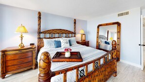 A spacious bedroom with a large bed, wooden headboard, bedside tables, and a mirror.