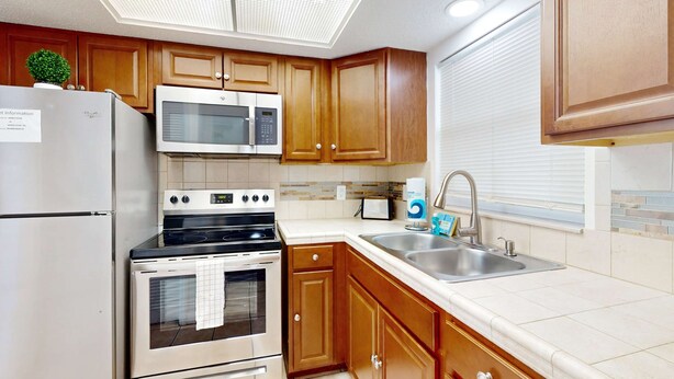 A kitchen with wooden cabinets, a stainless steel refrigerator, a microwave, an oven, and a sink. - Centrally located dog friendly comfortable home with AC and WD (Largo)
