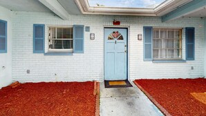 A white brick building with a blue door, two windows with blue shutters, and a red mulch ground cover. - Centrally located dog friendly comfortable home with AC and WD (Largo)