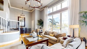 A spacious living room with a large window, a chandelier, a sofa set, and a coffee table. - Dog Friendly Retreat w/Bay Views, Pool, Spa & Onsite Marina (Clearwater)