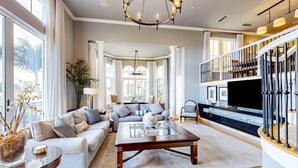 A spacious living room with a sectional sofa, a glass coffee table, and a large flat-screen TV. There is a staircase with a railing leading to an upper level. - Dog Friendly Retreat w/Bay Views, Pool, Spa & Onsite Marina (Clearwater)