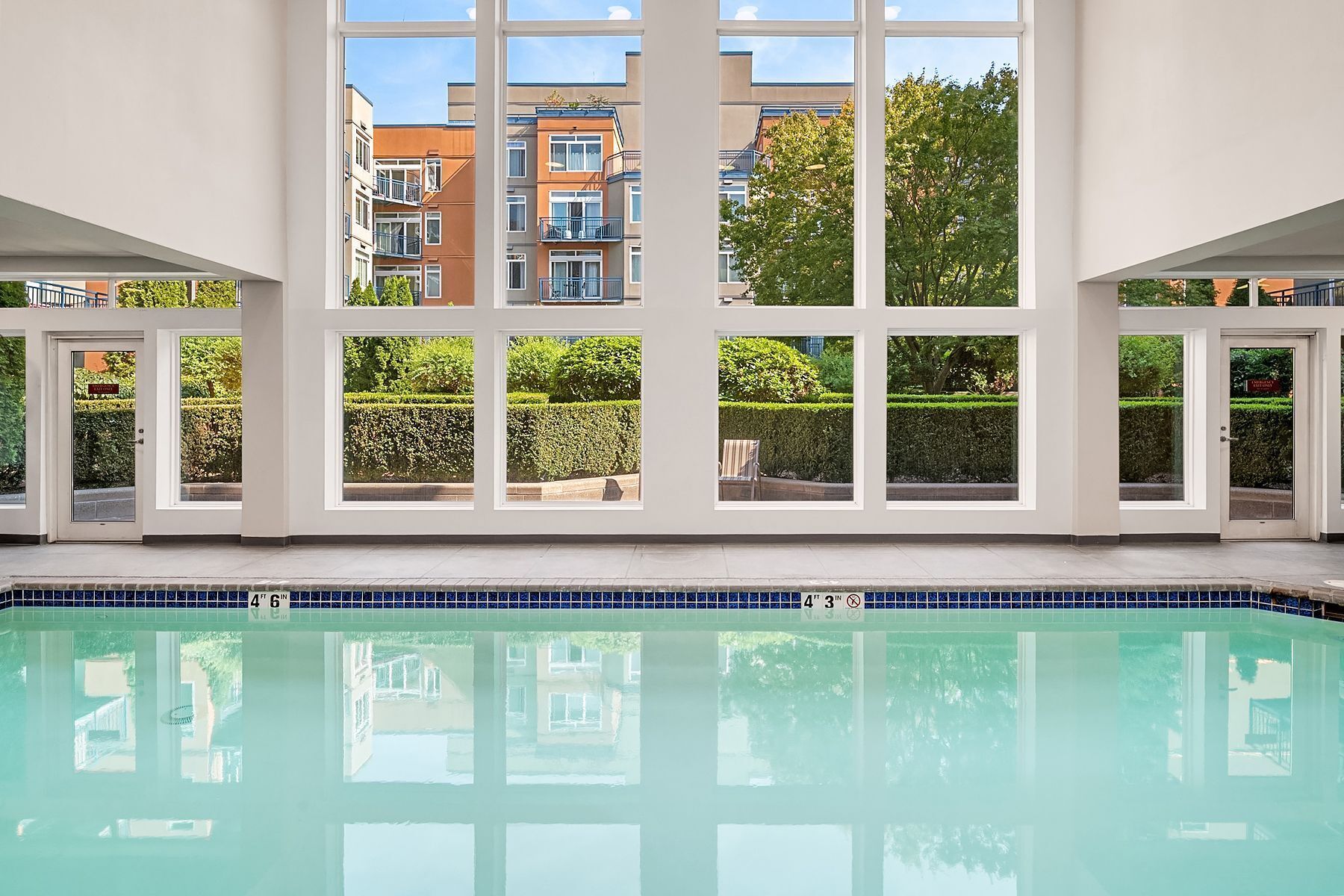 A swimming pool with clear blue water, surrounded by a white wall with multiple windows.
