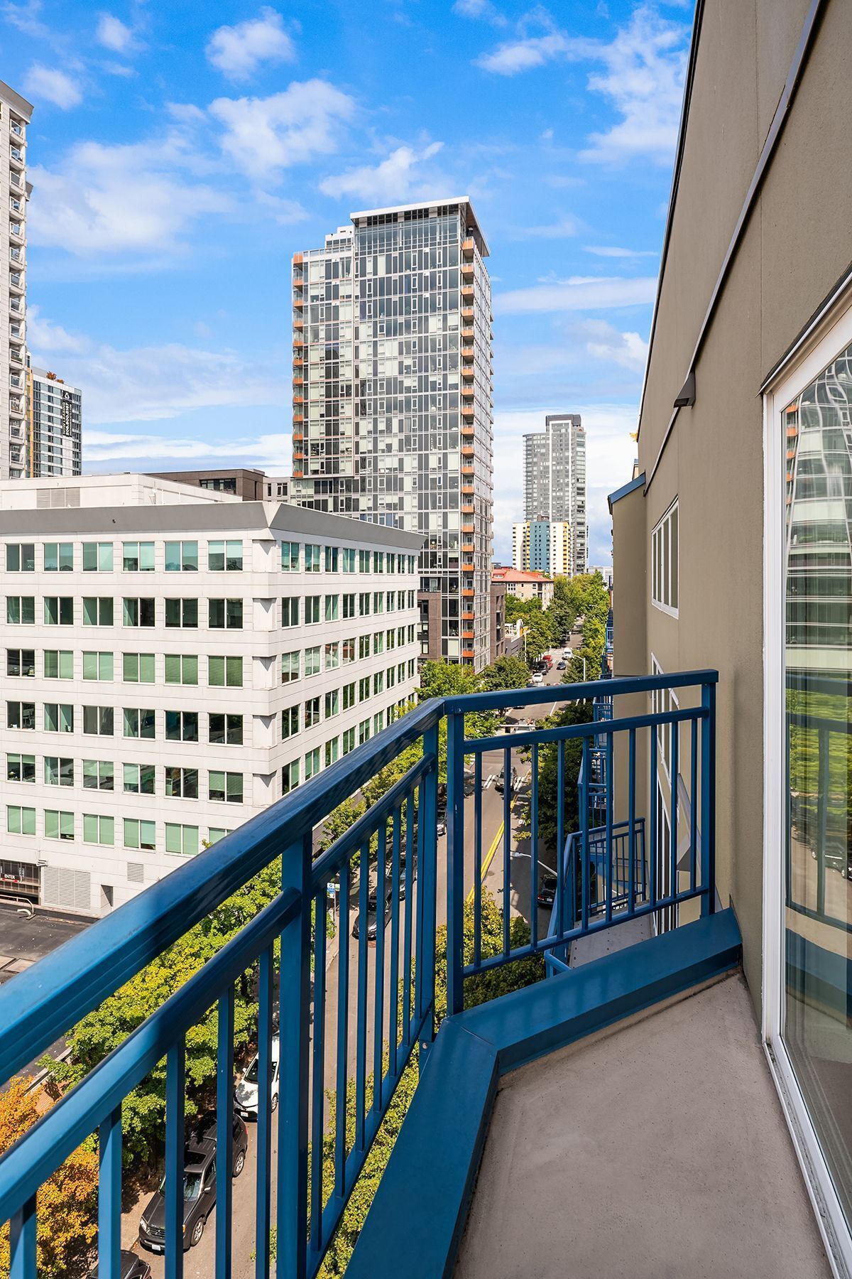 Un balcon doté d’une balustrade bleue, d’où l’on peut admirer un paysage urbain avec des bâtiments modernes.