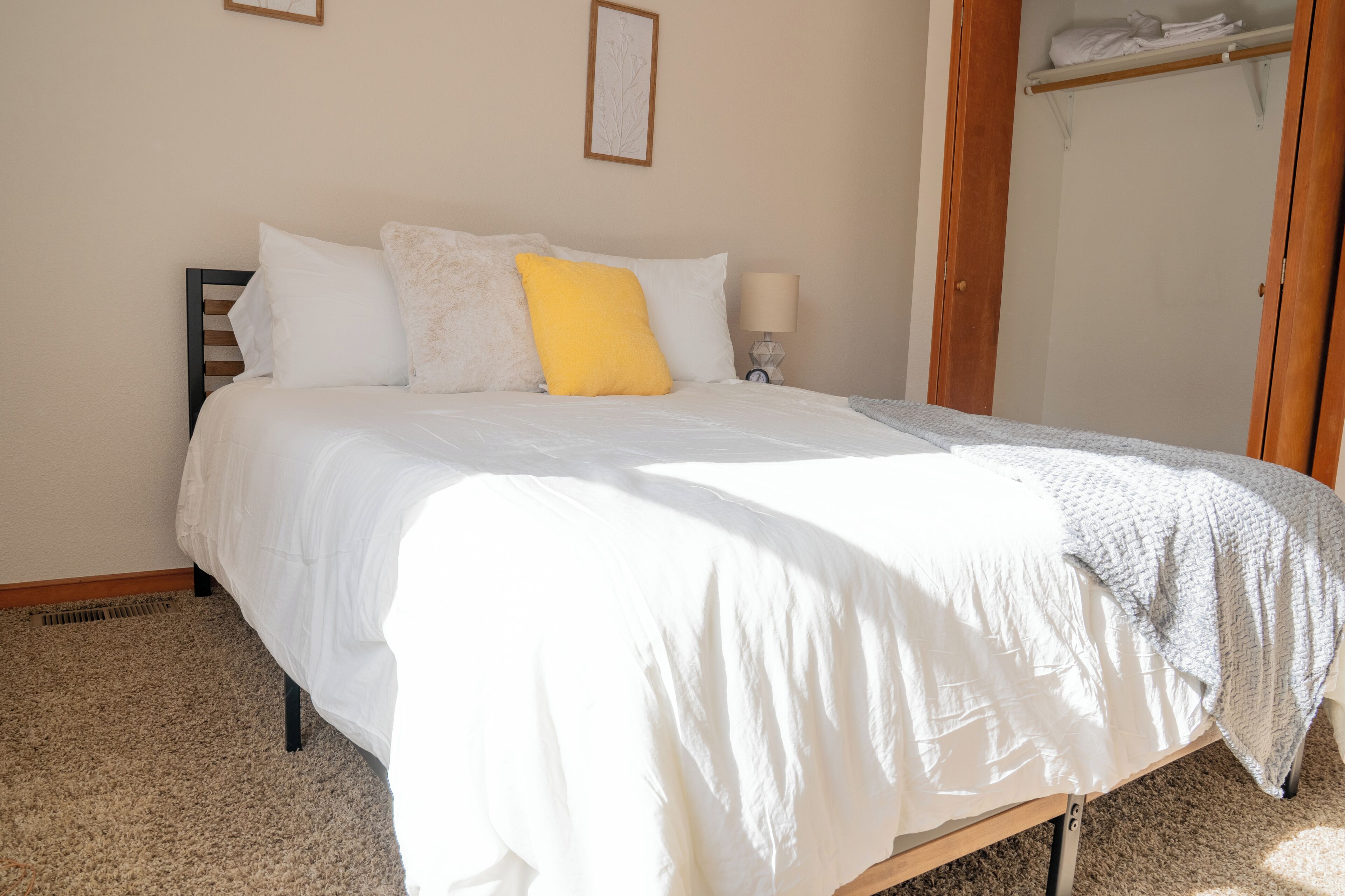 Ein ordentlich gemachtes Bett mit weißer Bettwäsche und einem gelben Kissen, ein Nachttischchen mit einer Lampe und ein Holzschrank im Hintergrund.