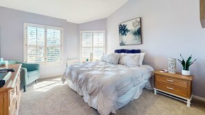 Un dormitorio con cama, cómoda, escritorio y ventanas.