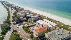 Ein Luftbild eines Küstenhotels mit Strandlage, das mehrere Gebäude, eine Straße und einen Yachthafen zeigt.