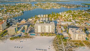 Oversigtsbillede af en kystby med et markant hotel med flere etager, en strand med liggestole og en lysthavn med både.
