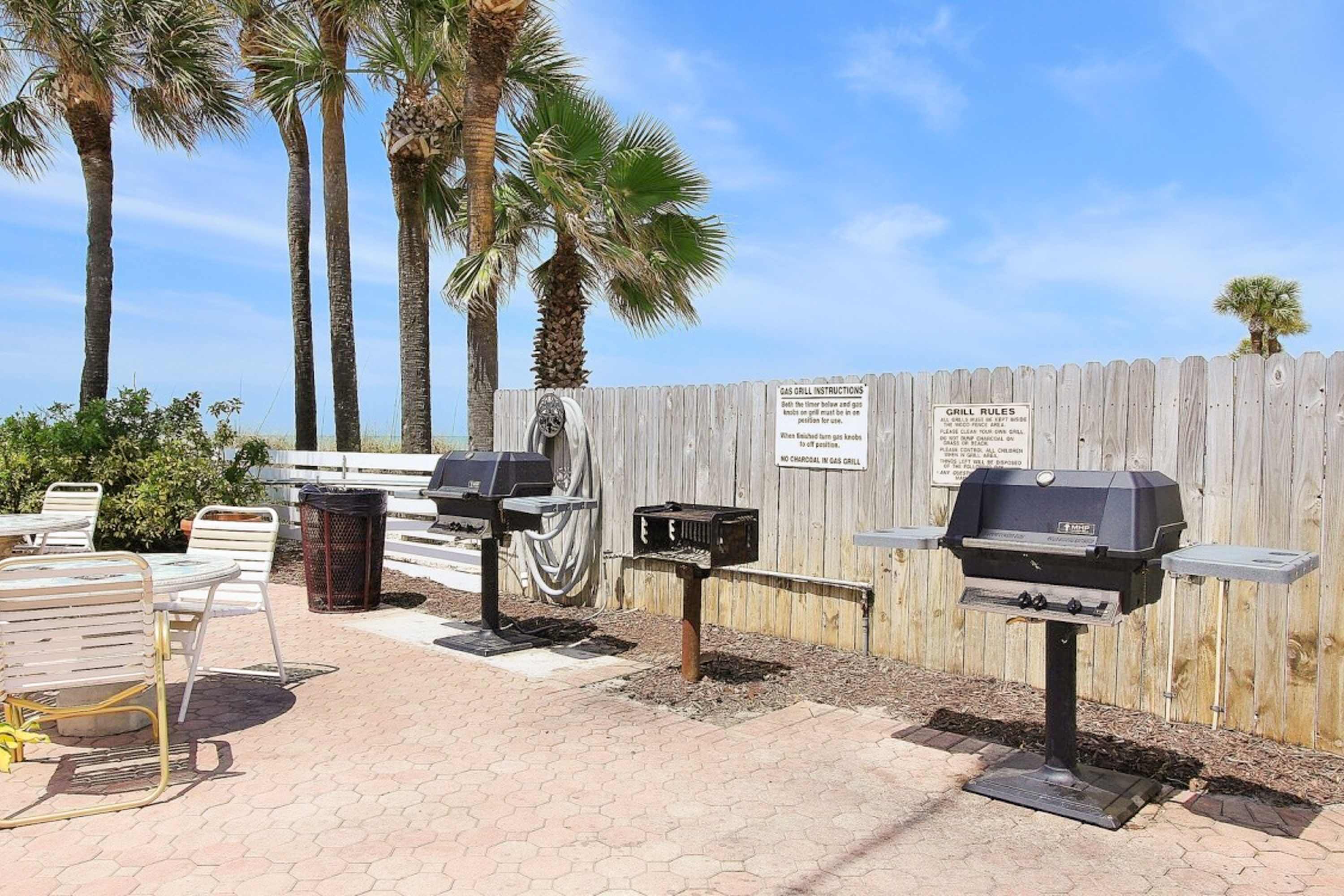 An outdoor patio area with two gas grills, a wooden fence, and palm trees.