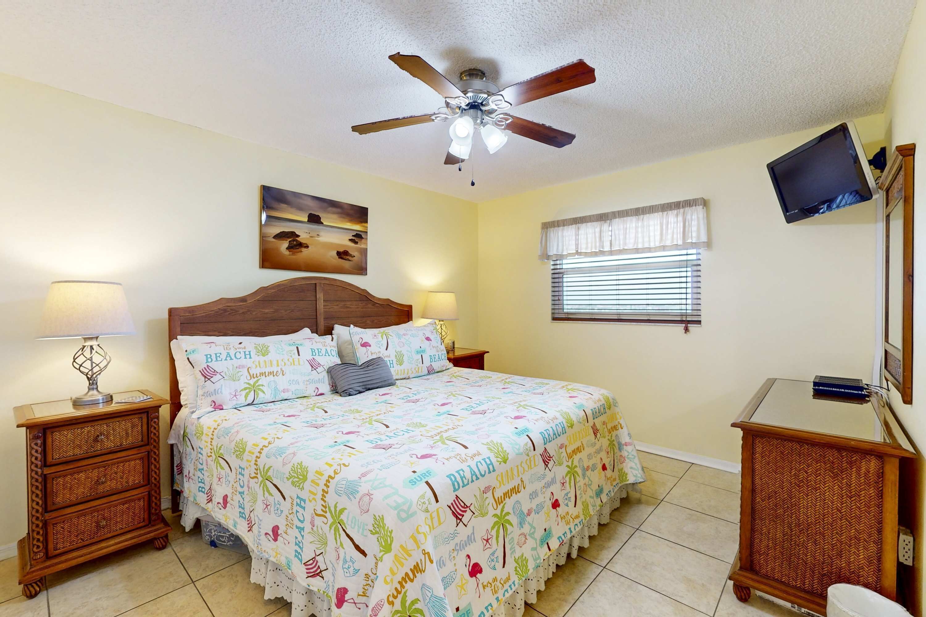 A bedroom with a bed, a ceiling fan, a nightstand, a dresser, a television, and a window with blinds.