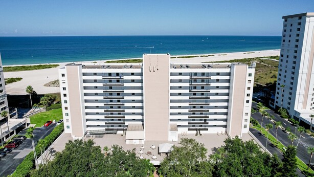 A high-rise hotel with a beach view, multiple floors, and a parking area. - Second floor condo with pool and tennis court private WD and central AC (Clearwater)