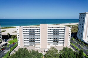 Een hoog hotel met uitzicht op het strand, meerdere verdiepingen en een parkeerplaats.