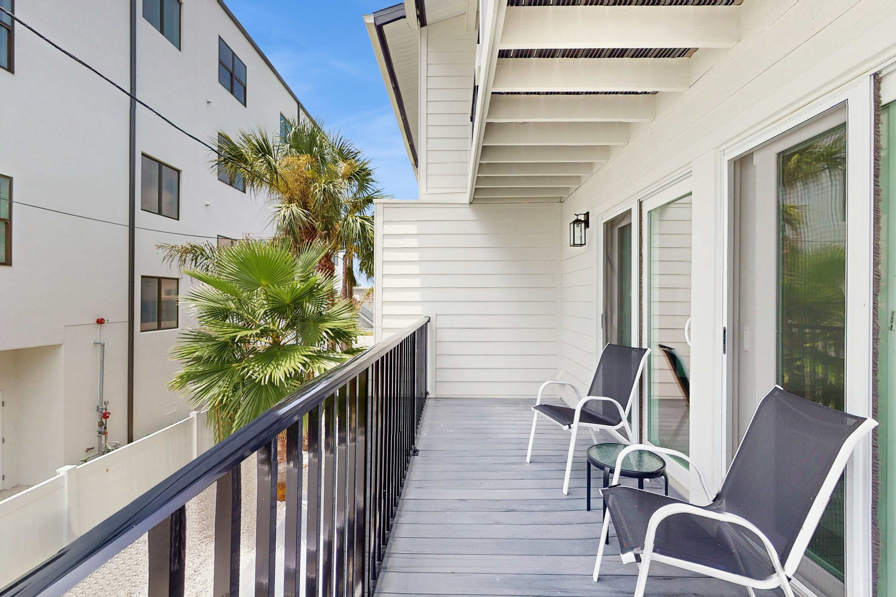 A balcony with a railing, two chairs, and a palm tree.