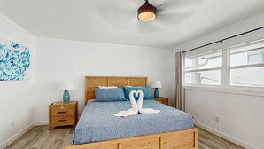 Une chambre à coucher avec un lit en bois, un ventilateur de plafond, une table de chevet avec une lampe et une fenêtre avec des rideaux.