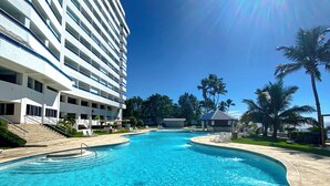 A swimming pool with clear blue water, surrounded by a modern building with multiple floors and balconies. - Charming 2-bedrooom Apartment with Majestic Ocean & Pool View in Juan Dolio (Juan Dolio)