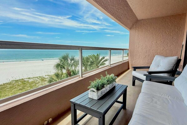 A balcony with a view of the beach, a sofa, a small table, and a planter box.