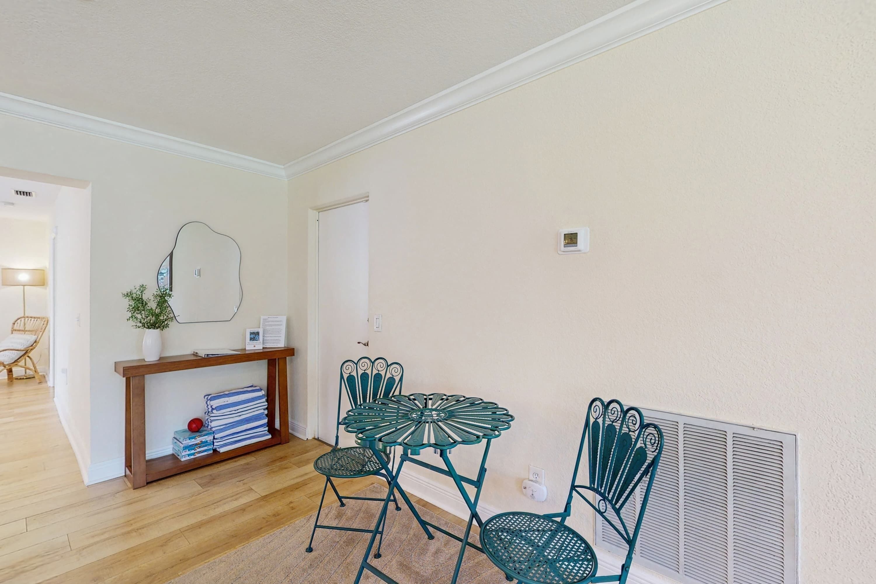 Uma área de refeições com uma mesa e cadeiras de metal verde, um aparador de madeira com um vaso e livros, e um radiador na parede.