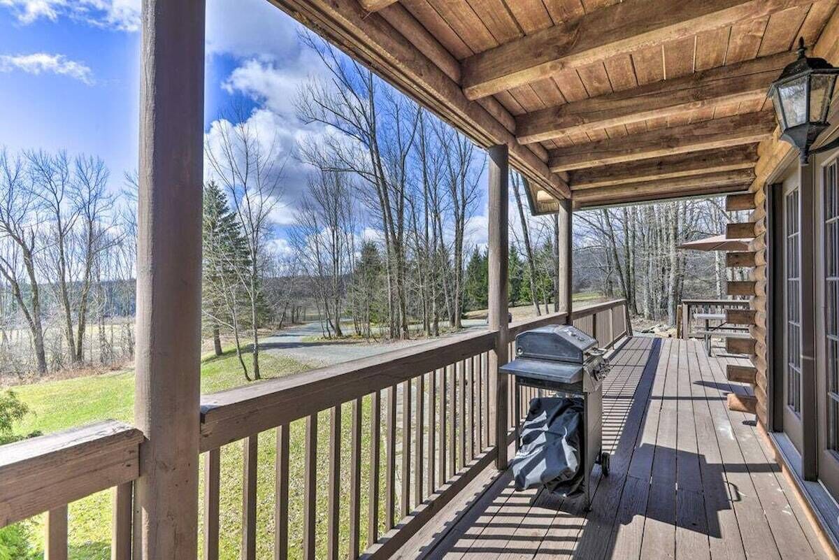 A wooden deck with a grill and outdoor seating, overlooking a grassy area and trees.