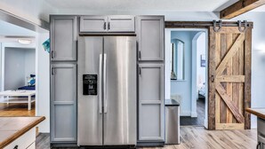 Une cuisine moderne dotée d’un réfrigérateur en acier inoxydable, de meubles en bois et d’une porte de style rustique rappelant celles que l’on trouve dans les granges.