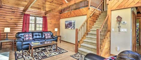 A log cabin interior with a living room, a staircase, and a fireplace.