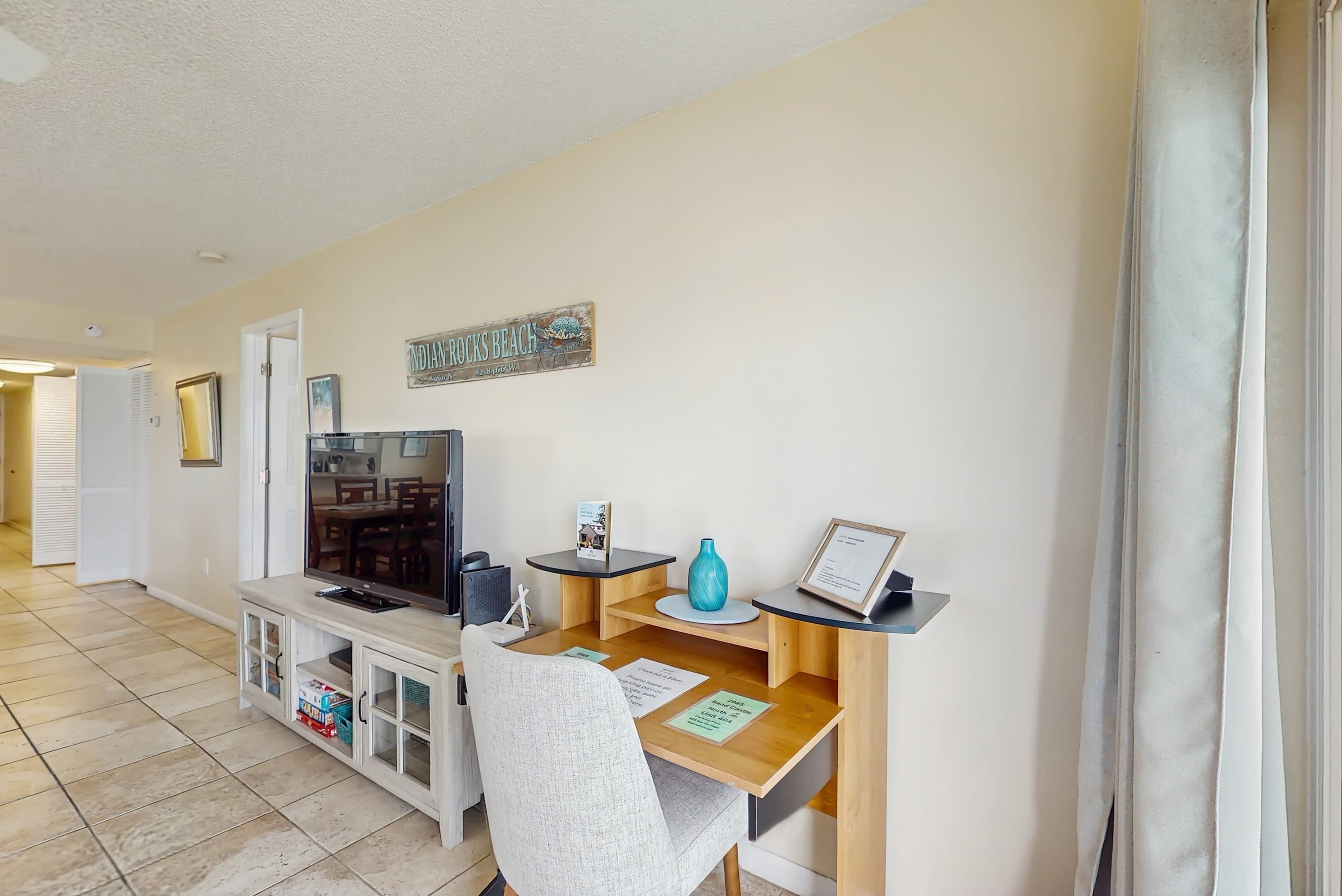 A living room with a TV, a small table, a chair, and a sign on the wall.
