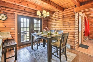 A wooden cabin interior with a dining table set for four, a chandelier, and a clock on the wall.