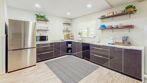 Una cocina moderna con armarios oscuros, electrodomésticos de acero inoxidable y estanterías integradas.