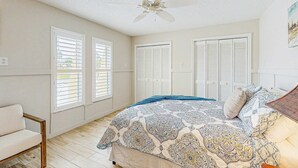 Un dormitorio con cama, ventilador de techo y ventana con persianas.