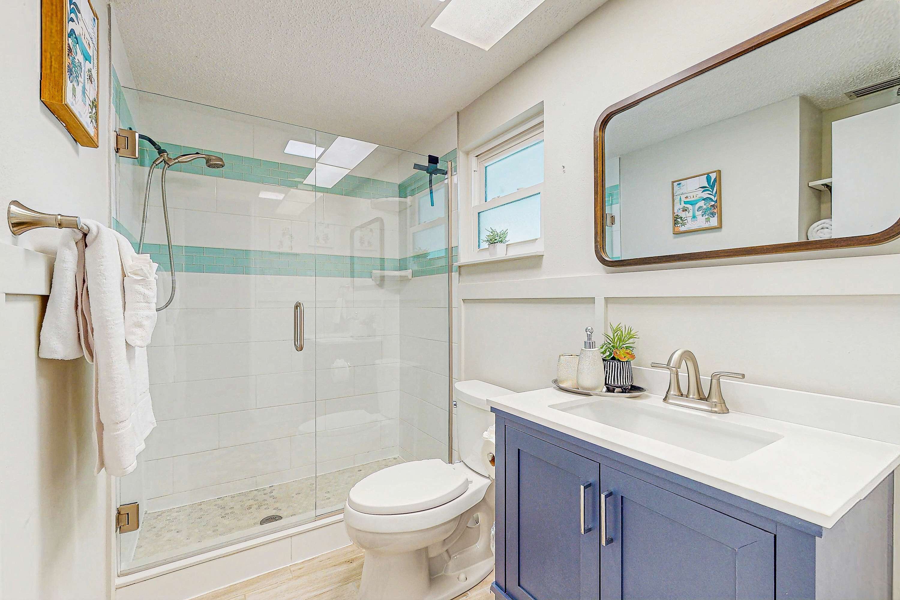 A modern bathroom with a glass-enclosed shower, a white toilet, a sink with a blue cabinet, and a mirror above the sink.