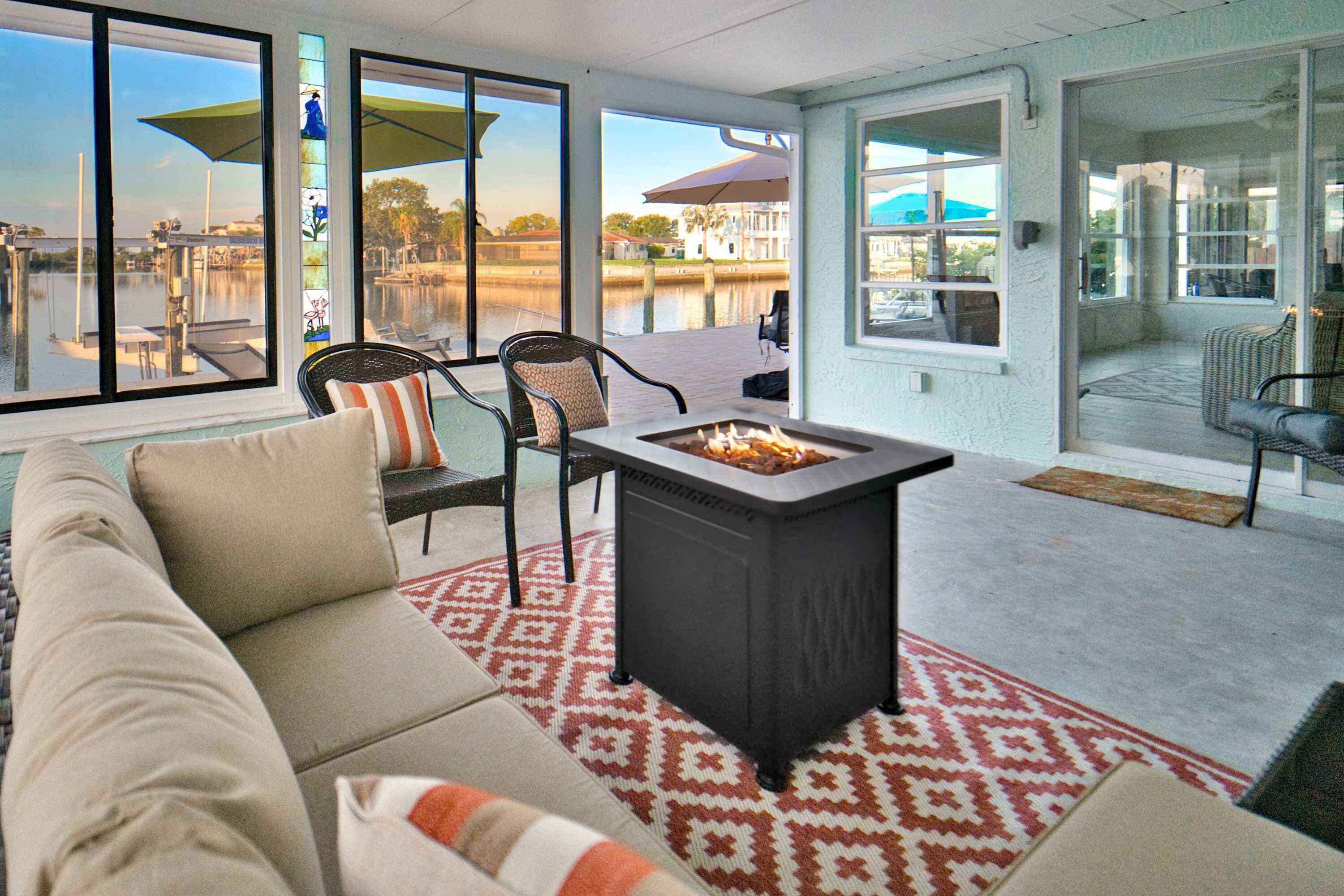 A covered patio with a fire pit, seating area, and large windows overlooking a body of water.