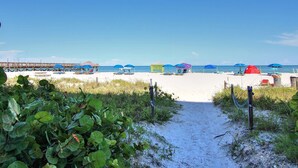 A beach path leading to beach umbrellas and a pier. - Corner beach condo with Gulf views beachside Pool and Hot tub (Indian Shores)