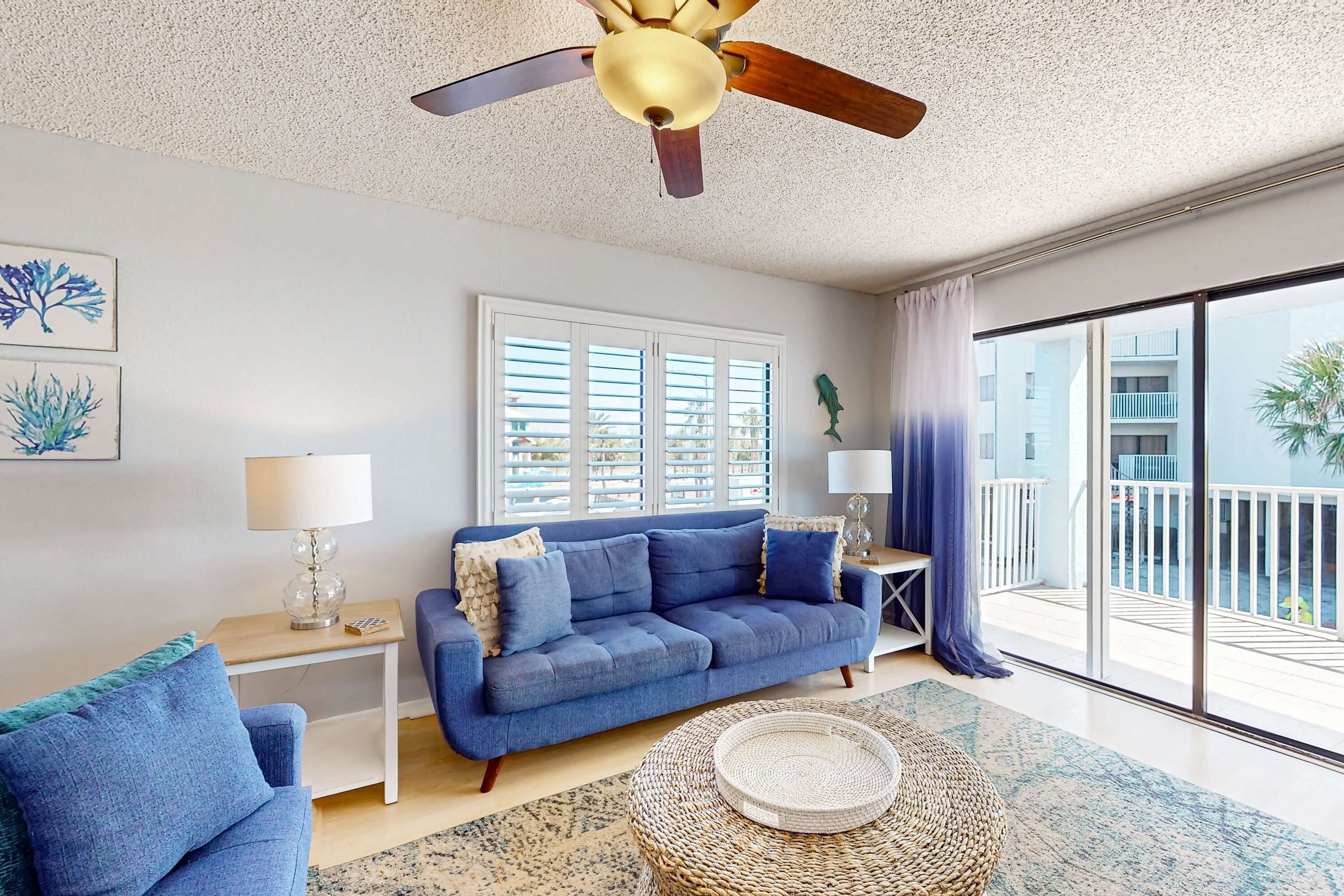A living room with a blue sofa, a round woven coffee table, and a ceiling fan.