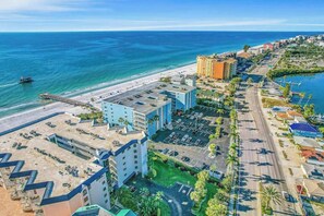 A coastal hotel with multiple buildings, a parking lot, and a beach view.