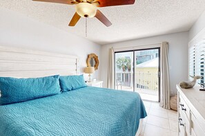 A bedroom with a large bed, a ceiling fan, a view of the outside balcony, and a white dresser.