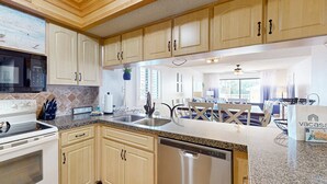 A modern kitchen with wooden cabinets, a stainless steel dishwasher, and a granite countertop. - Corner beach condo with Gulf views beachside Pool and Hot tub (Indian Shores)