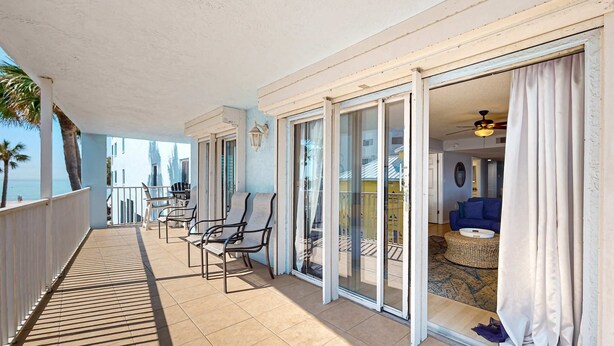 A balcony with a view of the ocean, a dining area with chairs, and a living room with a sofa and a round table. - Corner beach condo with Gulf views beachside Pool and Hot tub (Indian Shores)