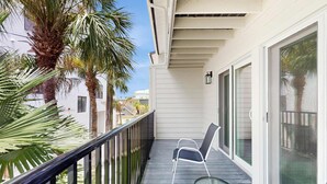 A balcony with a chair and table, palm trees, and a white building with large windows. - Modern dog friendly townhome close to the Gulf and beaches shopping and dining (Treasure Island)