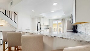 A modern kitchen with a marble countertop, bar stools, and a staircase. - Modern dog friendly townhome close to the Gulf and beaches shopping and dining (Treasure Island)