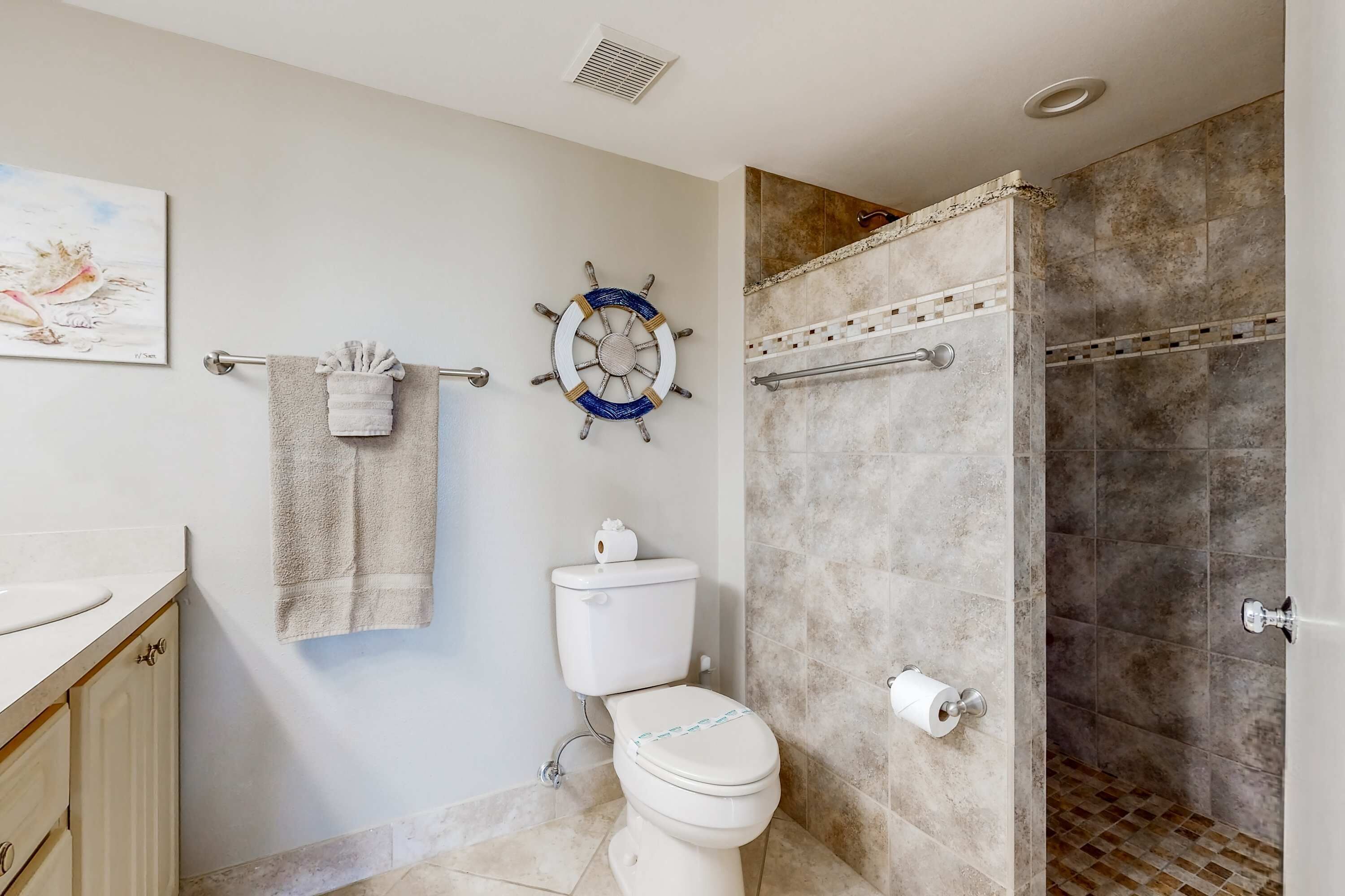 Un baño con inodoro, perchero, decoración de timón de barco y zona de ducha.