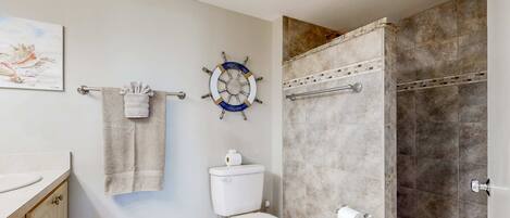 Un baño con inodoro, perchero, decoración de timón de barco y zona de ducha.