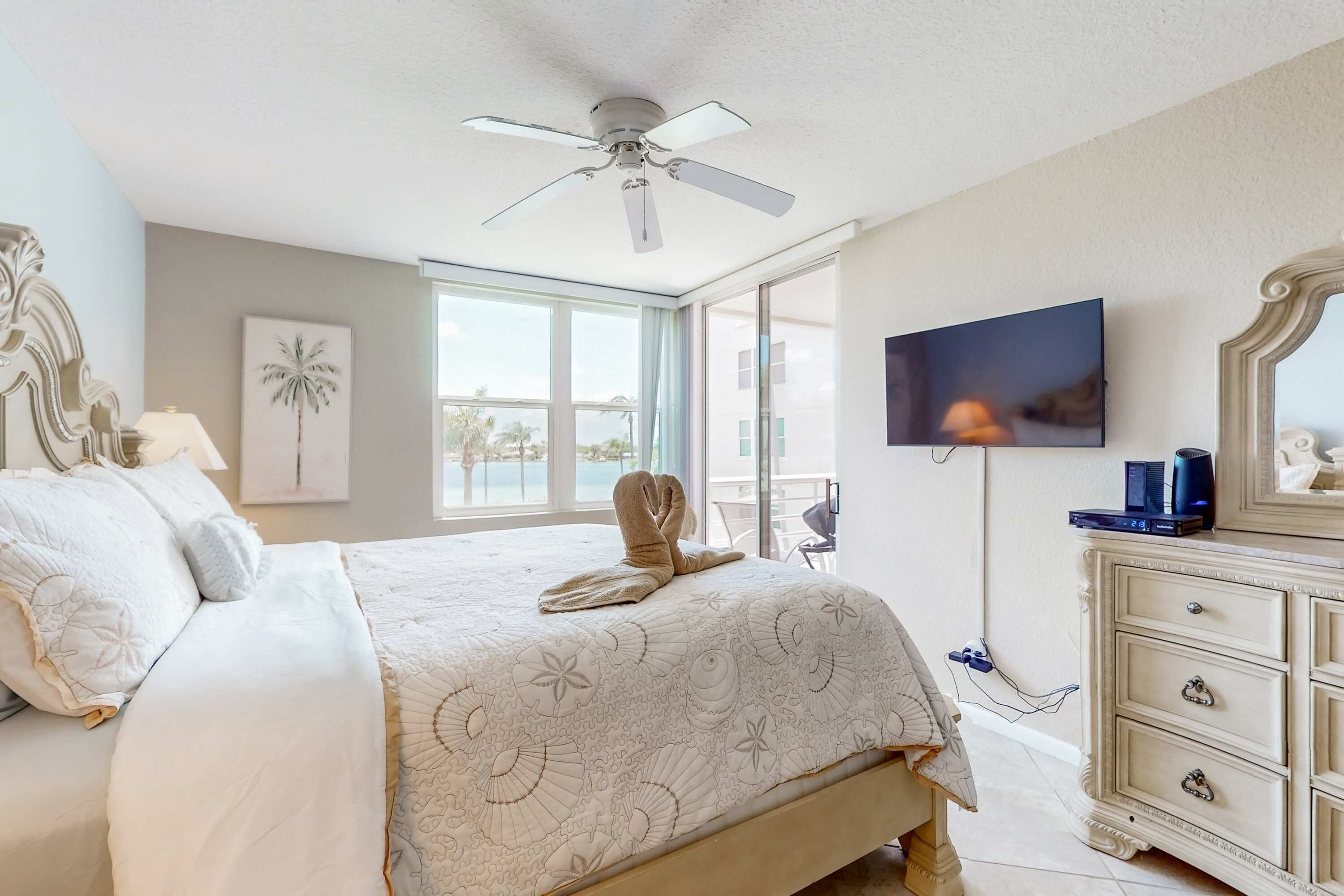 A bedroom with a bed, a ceiling fan, a TV, and a dresser.