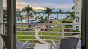 Ein Balkon mit Blick auf einen Pool, Palmen und ein Gebäude gegenüber dem Wasser.