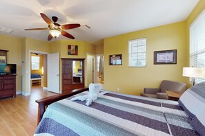 A hotel room with a bed, a ceiling fan, a television, a desk, and a chair.