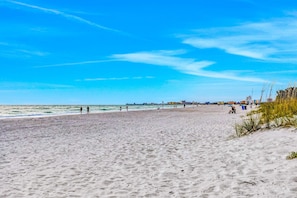 A beach with a clear sky, sandy shore, and distant buildings.