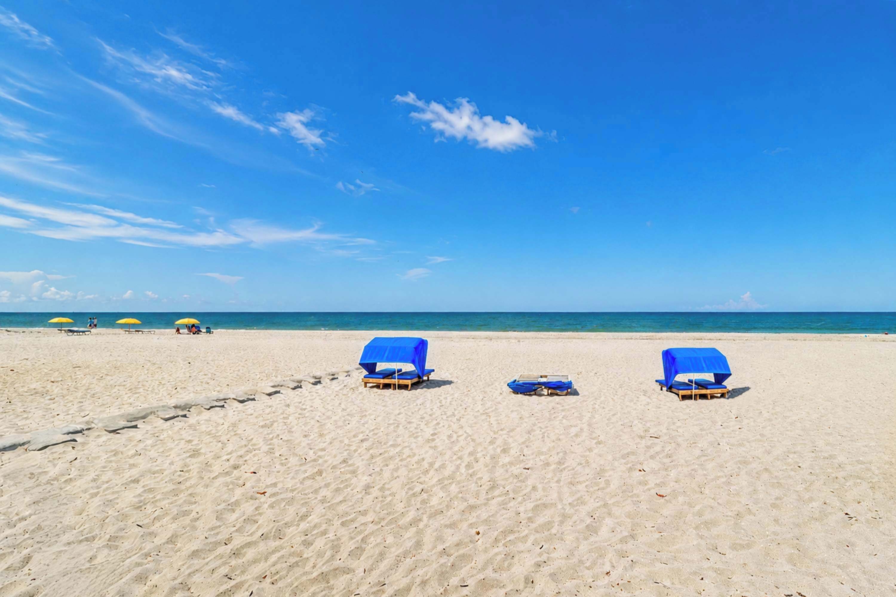 A beach with three blue lounge chairs and a pair of yellow umbrellas.