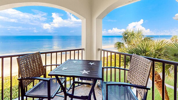 A balcony with a table and chairs, overlooking a beach and ocean. - Gulf front penthouse on Belleair Beach (Belleair Beach)