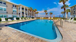 A swimming pool with lounge chairs and palm trees, surrounded by a multi-story building with balconies. - Gulf front penthouse on Belleair Beach (Belleair Beach)