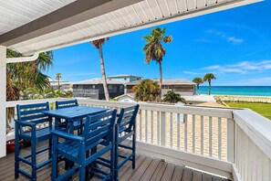 A wooden deck with blue chairs and a table, overlooking a beach with palm trees and a clear blue sky. - Delightful condo with beach and pool access washer dryer (Belleair Beach)