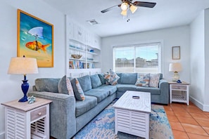 A living room with a grey sofa, a coffee table, a lamp, a bookshelf, and a painting of a fish. - Delightful condo with beach and pool access washer dryer (Belleair Beach)